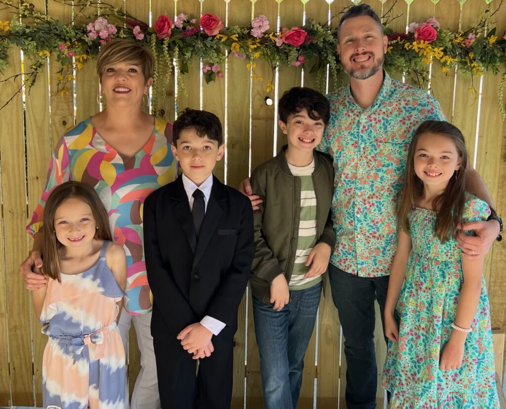 Josh Meadows poses with his wife and their 4 children in front of a wooden fence