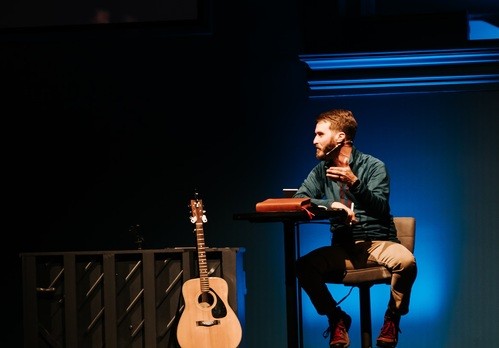 Cody Hale sitting in a chair on a stage teaching